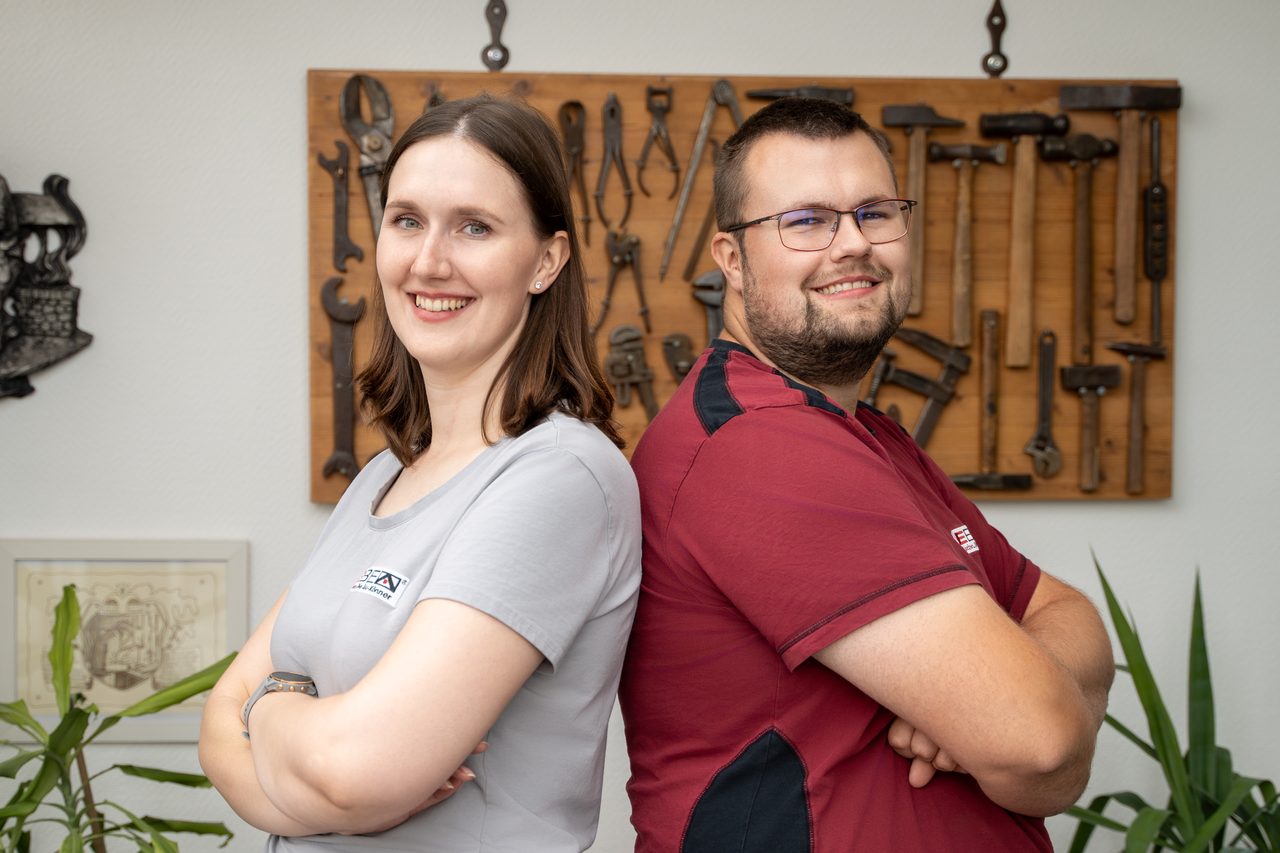 Maike Helena Eschen und Malte Eschen stehen Rücken an Rücken vor einer Wand mit altem Werkzeug