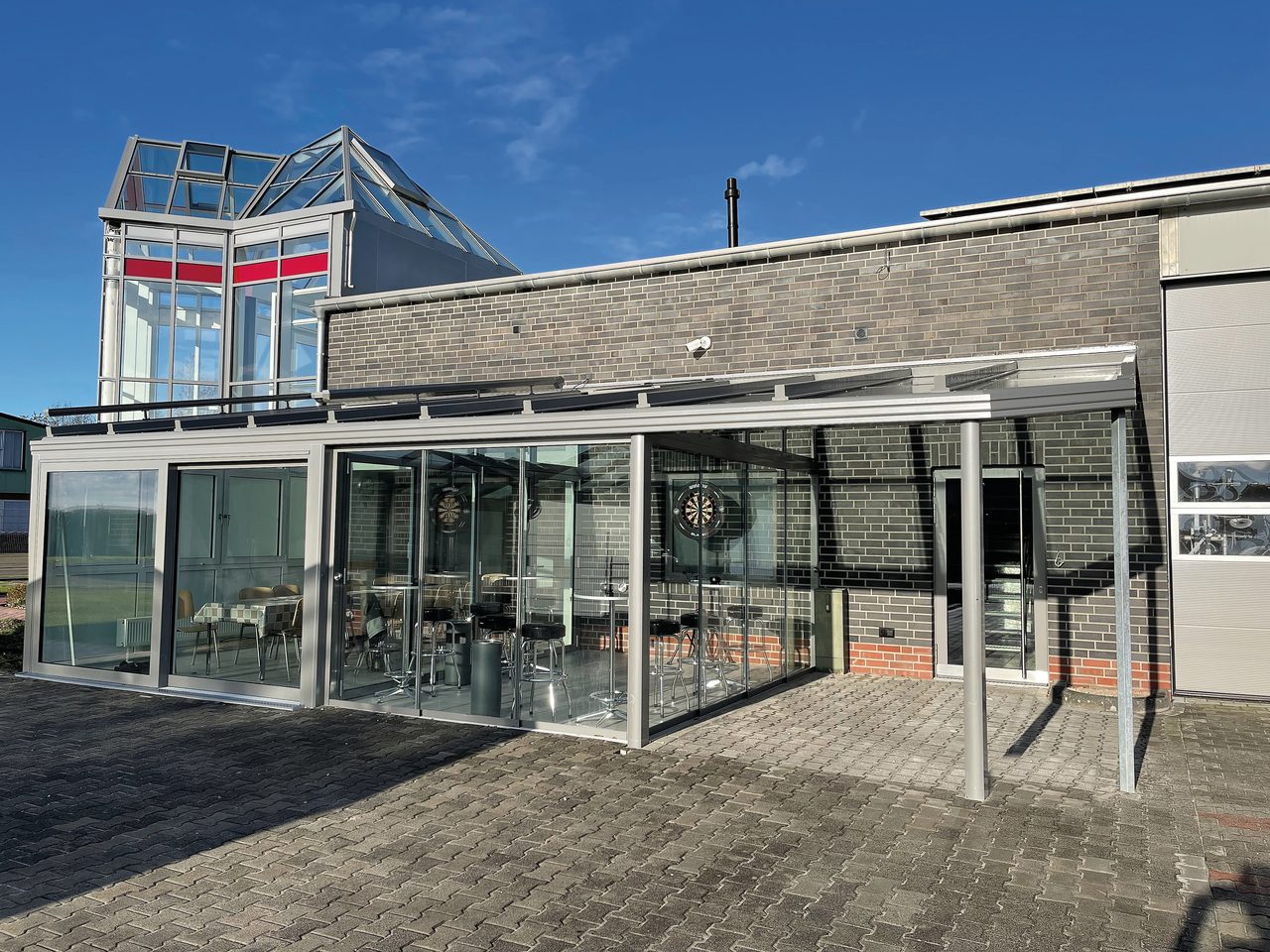 Sommergarten mit Glasschiebewänden unter einem anthrazitfarbenen Terrassendach am EBE-Gebäude