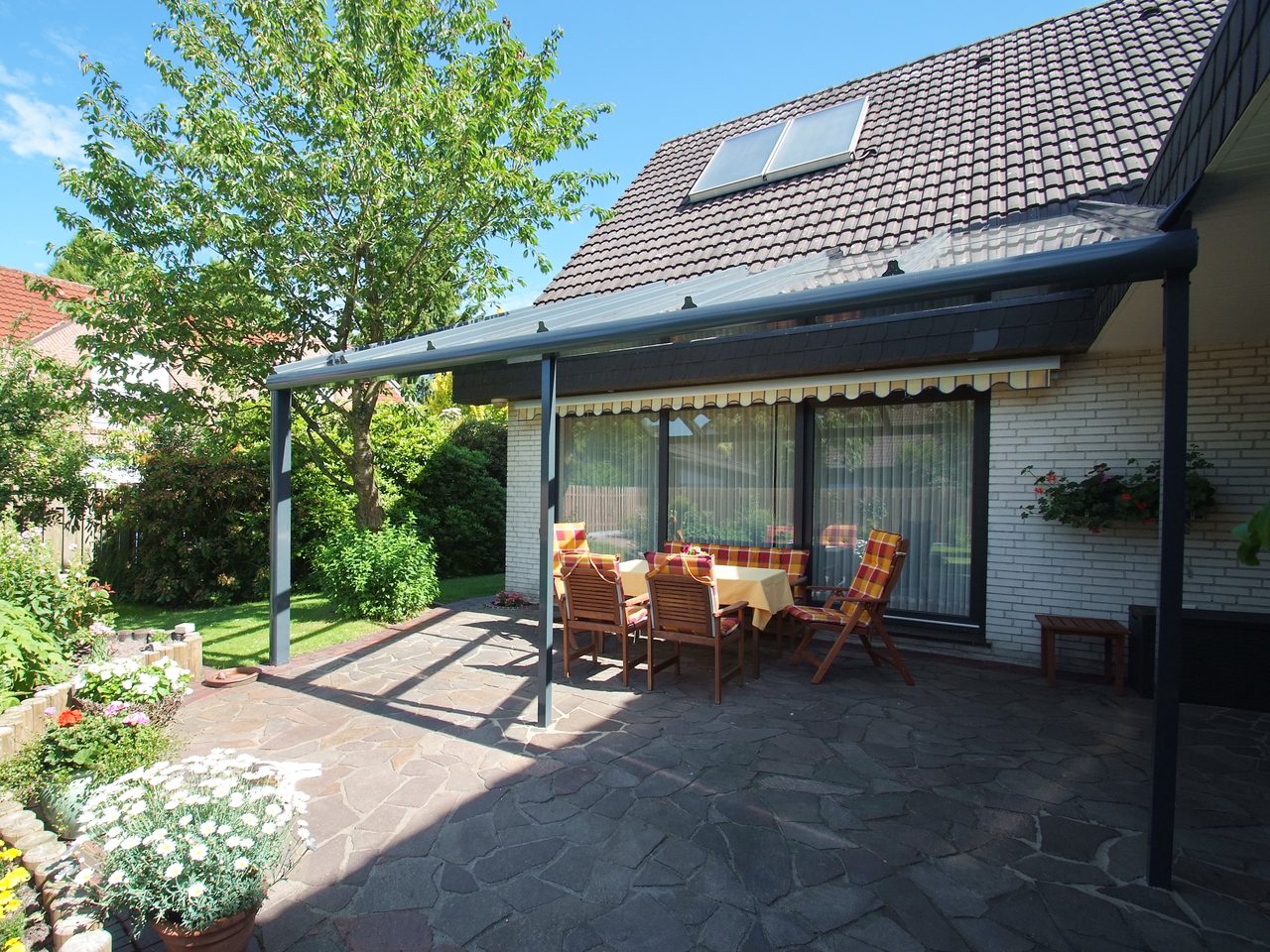 Anthrazitfarbene Terrassenüberdachung mit Glasdach an einem weißen Klinkerhaus